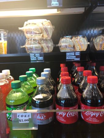 ham and cheese sandwiches and soda on a shelf in a refrigerated cabinet