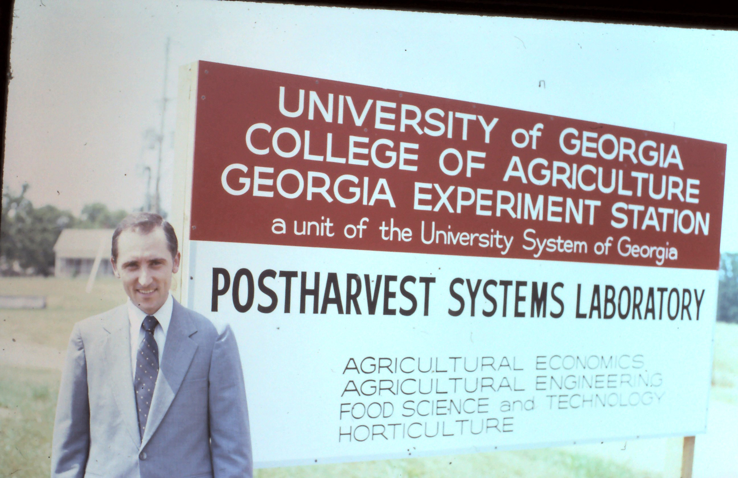 photo of the author next to a sign identifying Agriculutral Economics, Agricultural Engineering, Food Science and Technology and Horticulture as major players
